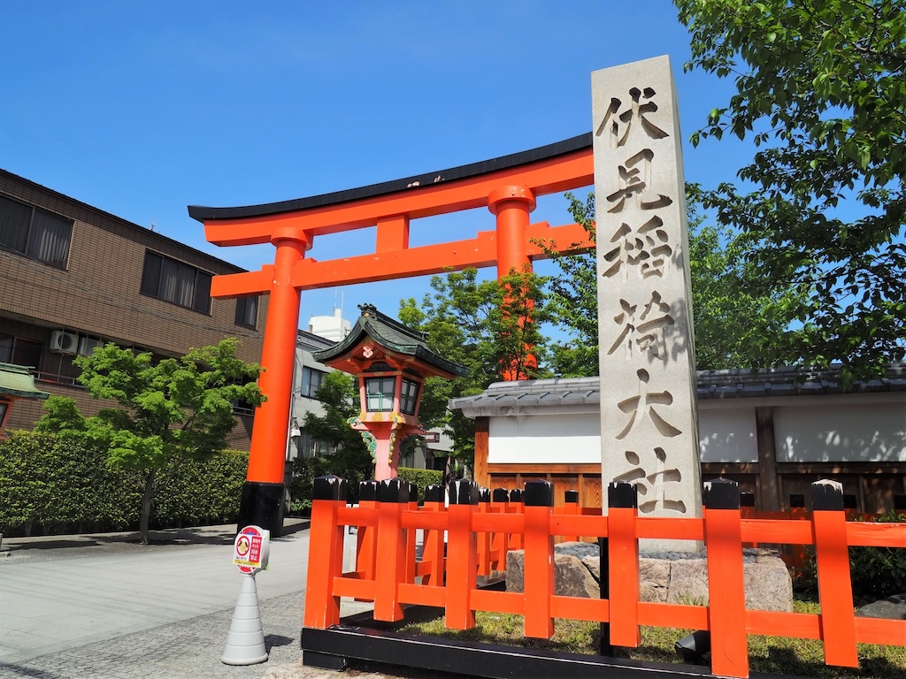 青空を背景に立つ伏見稲荷大社の社号標石柱と朱色の大鳥居