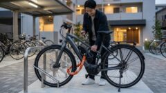 駐輪場で電動アシスト自転車のフレームと後輪にチェーンロックとU字ロックを装着し、防犯対策をする男性